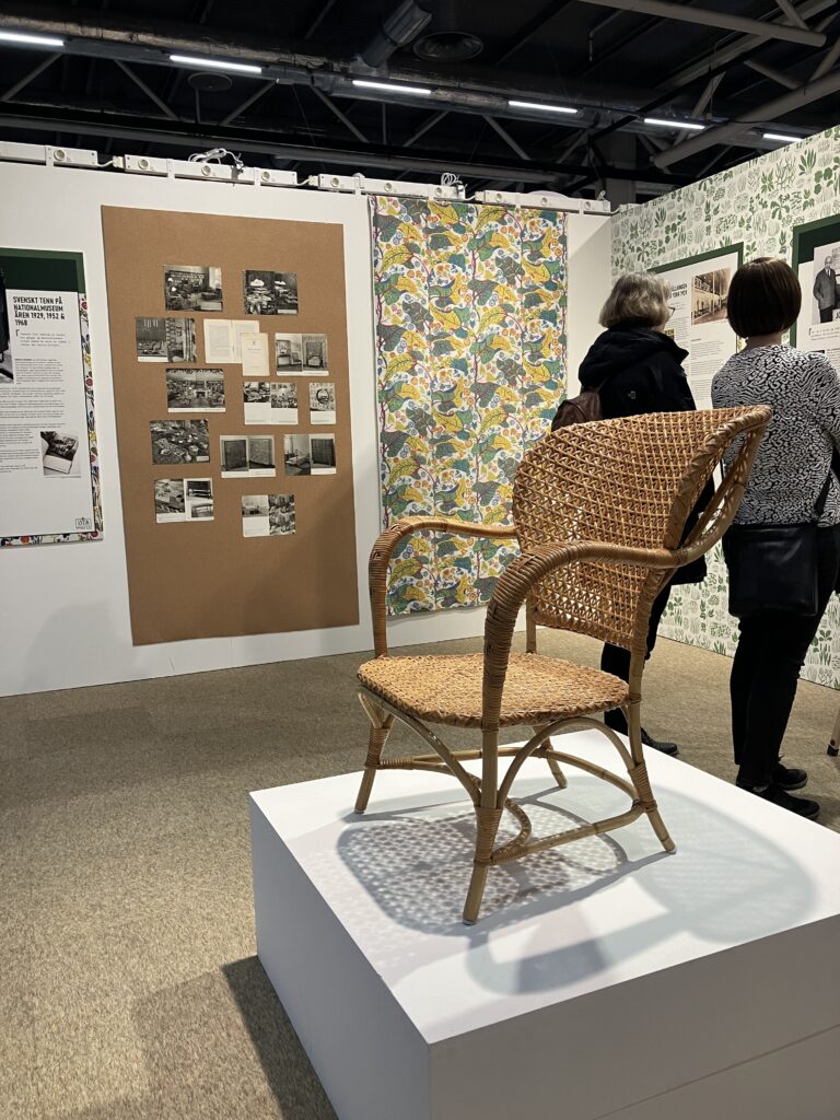 två personer står och tittar i en utställning med texter, bilder och föremål från Svenskt Tenn